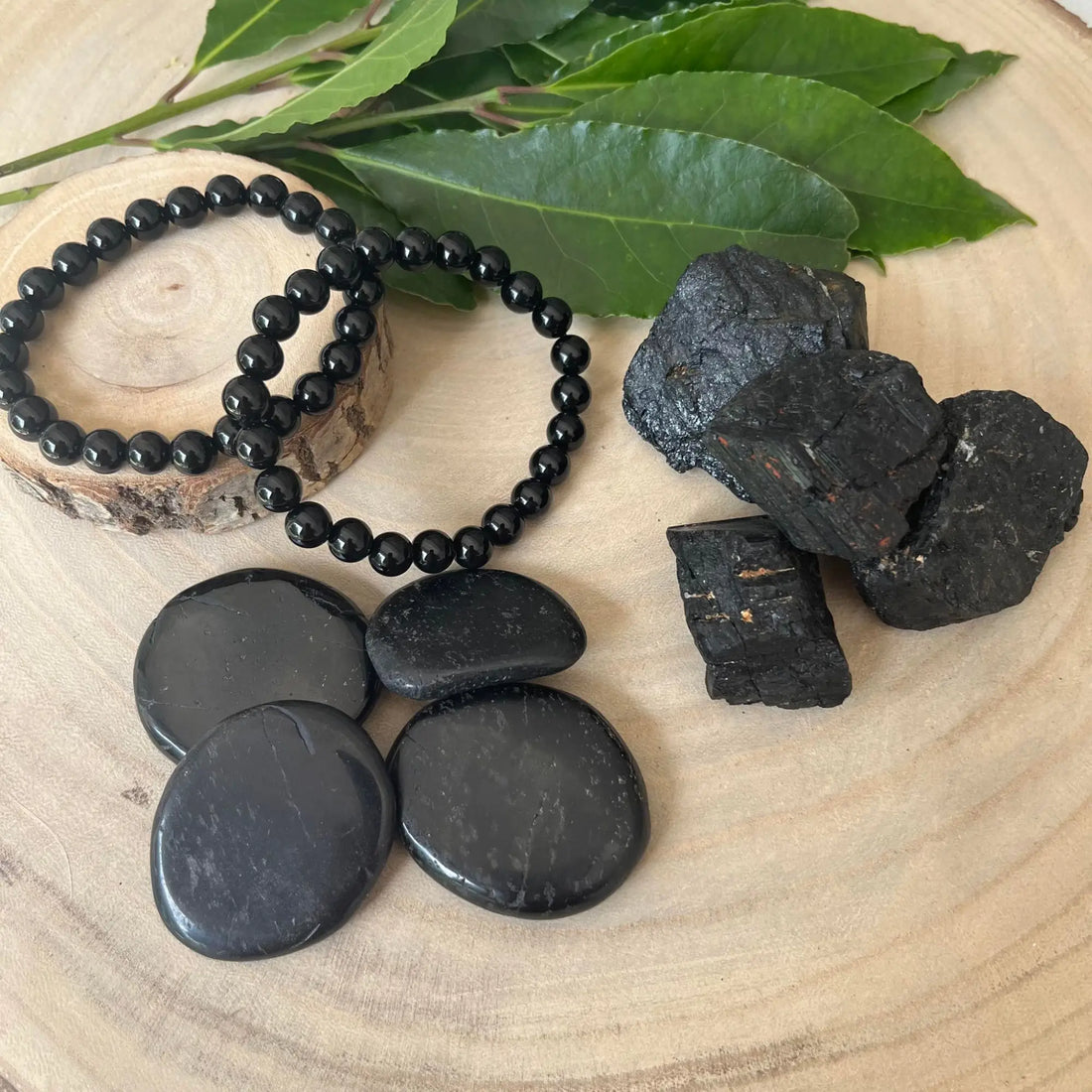 La tourmaline noire en bracelet, galets et pierres brutes sur un plateau en bois avec des feuilles