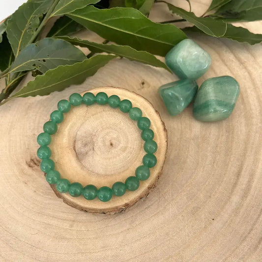 Bracelet Aventurine Verte Naturel fait de perles rondes sur un support en bois, avec des pierres assorties en arrière-plan.