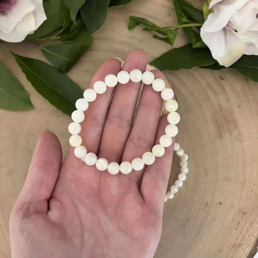 Bracelet en Nacre Naturelle de perles blanches rondes porté à la main sur fond naturel avec fleurs