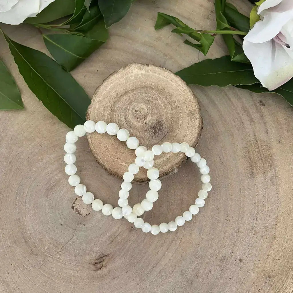 Bracelet en Nacre Naturelle Aura de Roche perles rondes blanches posé sur bois avec feuilles vertes