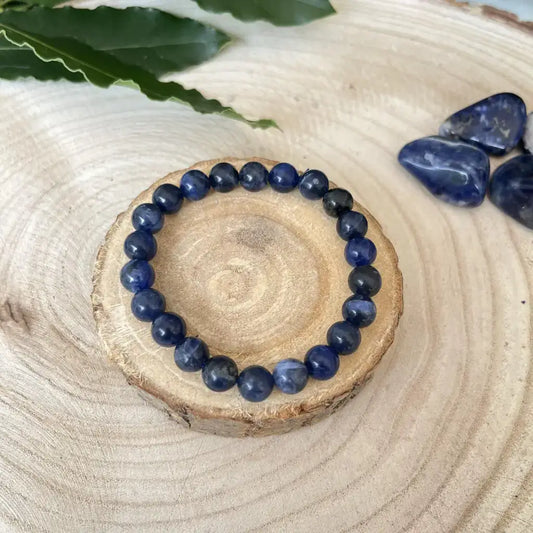 Bracelet Sodalite Naturelle – Pierre de Sagesse et d’Expression sur un support en bois, avec des pierres de sodalite à côté