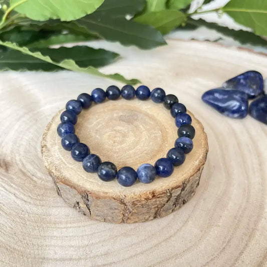 Bracelet Sodalite Naturelle – Pierre de Sagesse et d’Expression sur un support en bois, entouré de pierres de sodalite