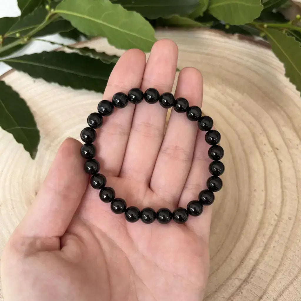 Bracelet Tourmaline Noire en perles brillantes sur une main avec des feuilles en arrière-plan