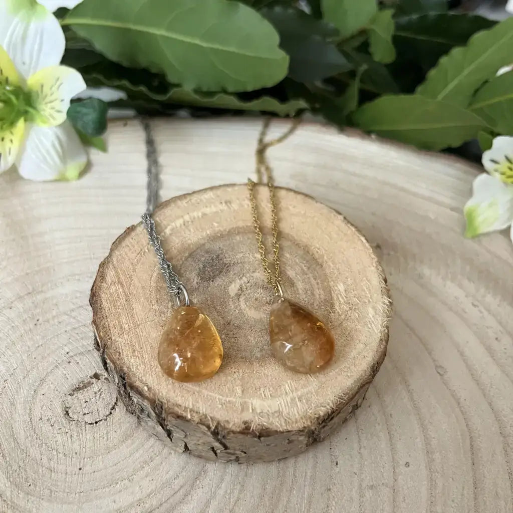 Collier avec Pendentif Citrine suspendu sur un support en bois avec des fleurs en arrière-plan