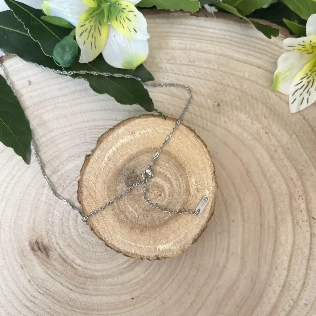 Collier Pierre de Lune Bleutée sur un support en bois avec des fleurs en arrière-plan