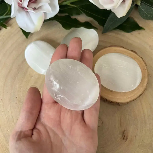 Galet en Sélénite naturel dans une main, mettant en avant sa texture et sa luminosité