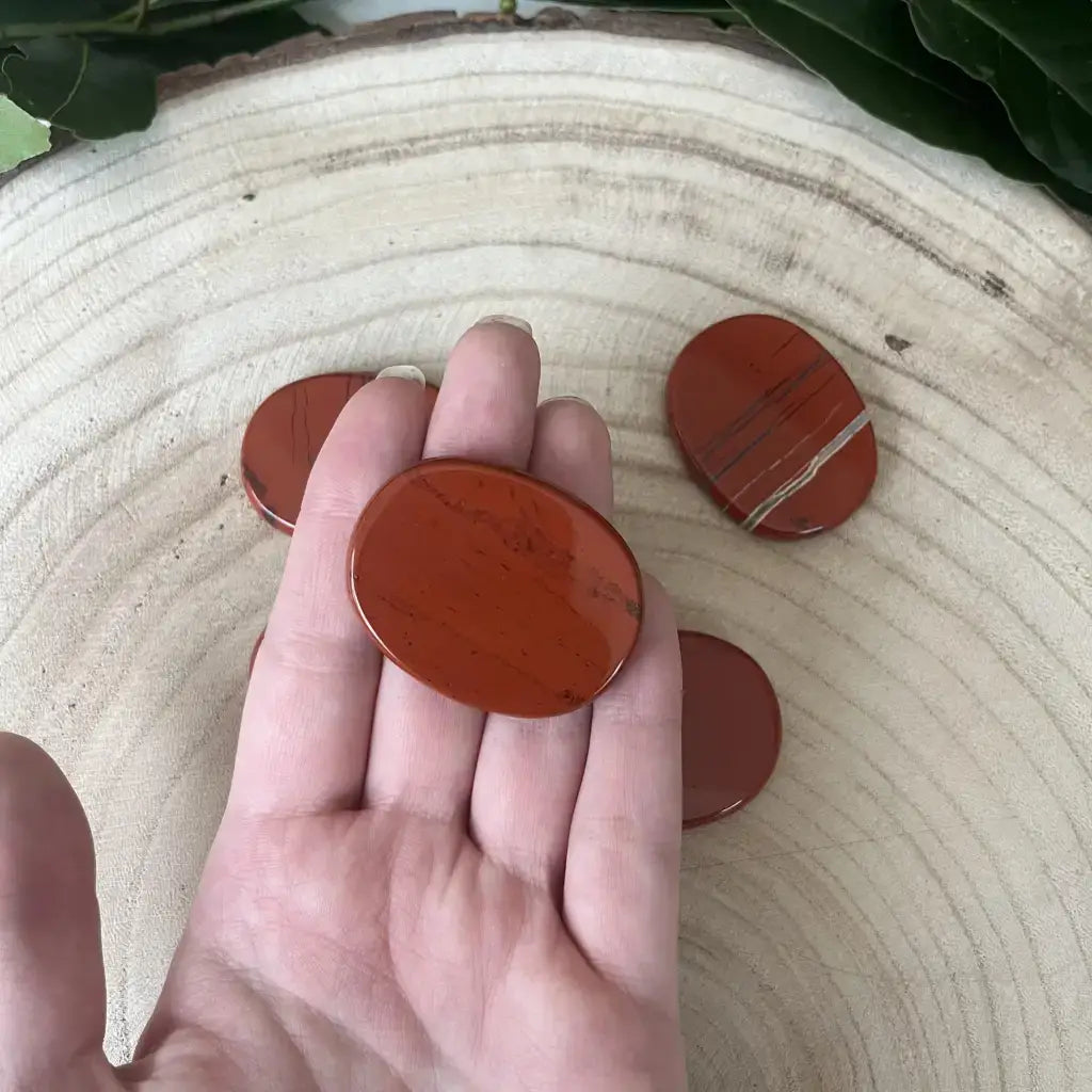 Galet Plat Jaspe Rouge lisse tenu dans la main sur tranche de bois pierres naturelles Aura de Roche