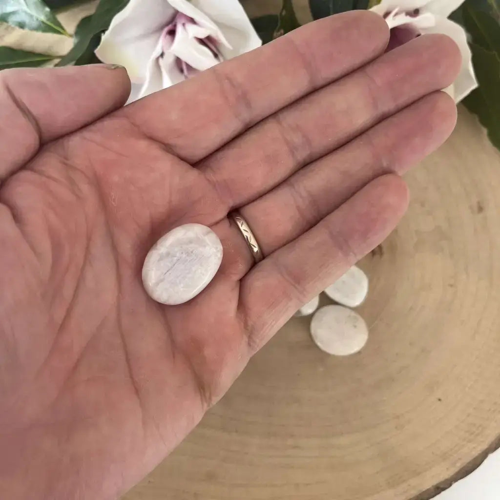 Main présentant un Mini Galet plat Pierre de Lune Bleutée lisse et irisé sur rondin de bois