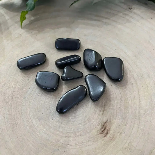 Mini Pierre Roulée Shungite en forme unique sur un fond en bois naturel, pierre protectrice idéale.