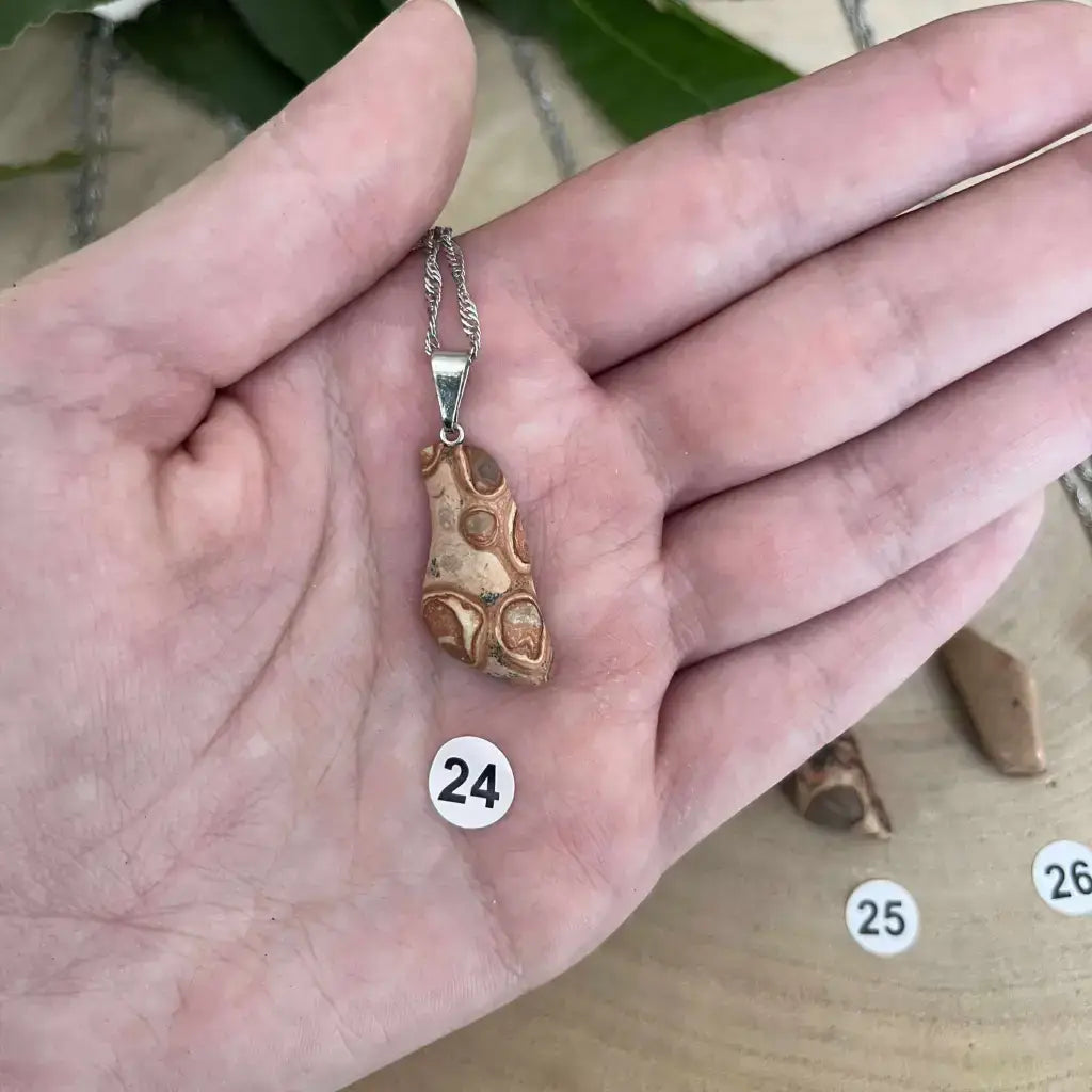 Pendentif Jaspe Léopard suspendu sur une chaîne en métal, présenté dans une main