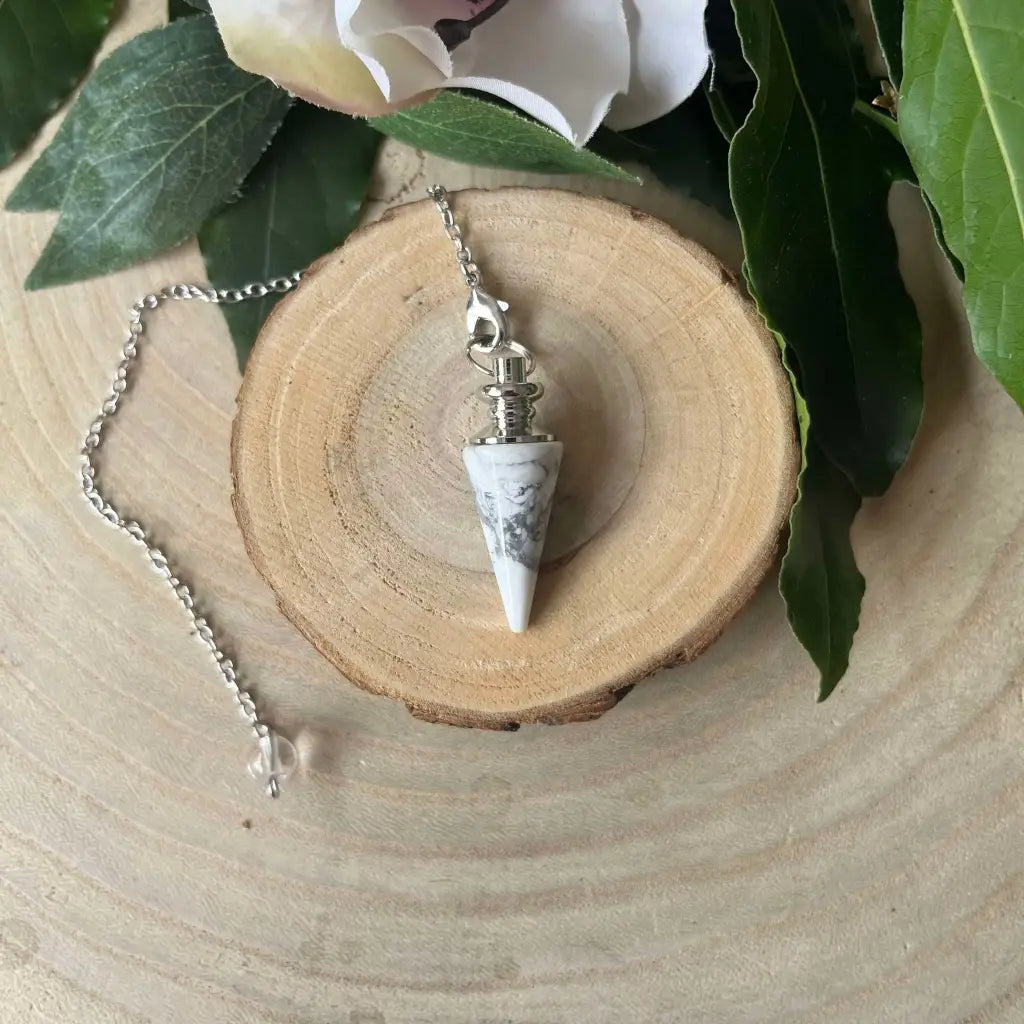 Pendule en Howlite Blanche Aura de Roche posé sur tranche de bois, pointe conique en pierre et chaîne argentée