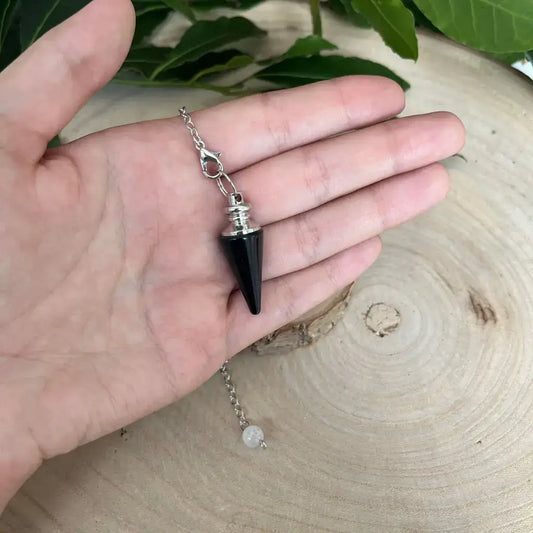 Pendule en Obsidienne Noire conique avec capuchon et chaîne argentée tenu dans la main sur bois Aura de Roche