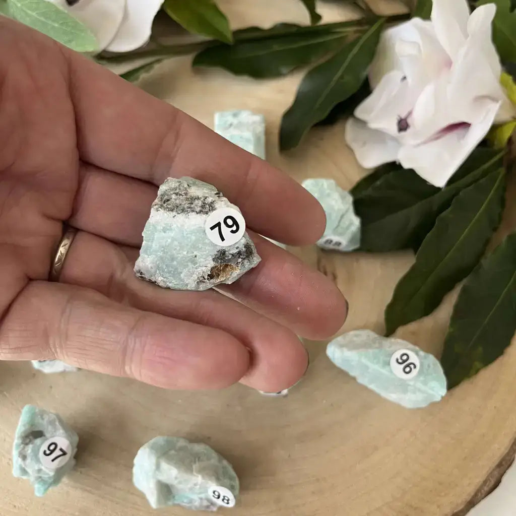 Pierre Brute Amazonite Brésil tenue dans une main avec d'autres pierres en arrière-plan