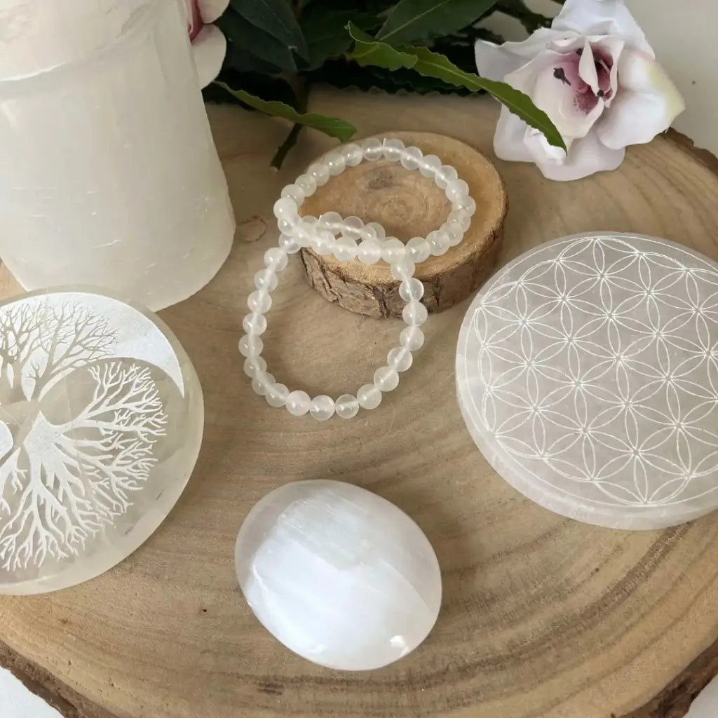 Plaque Fleur de Vie en Sélénite avec pierres et bracelet sur une table en bois naturel
