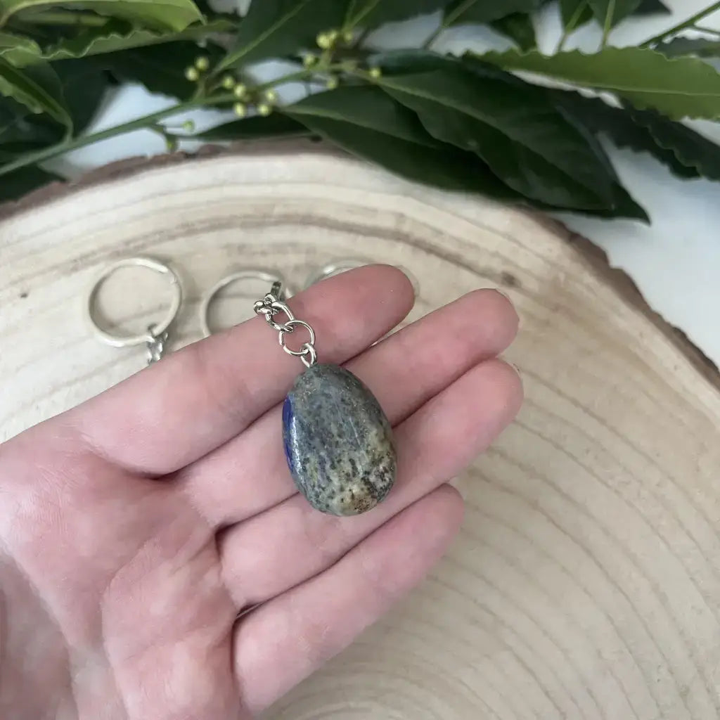 Porte clé Lapis Lazuli Naturel en main sur fond en bois, avec des feuilles en arrière-plan