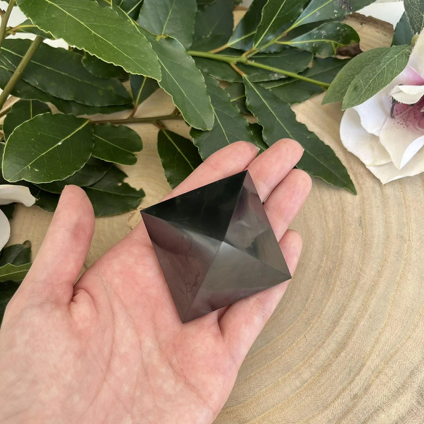 Main tenant une pyramide lisse en shungite gris foncé pour protection contre les ondes nocives coquille st jacques