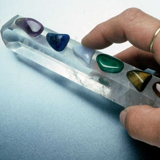 Comment choisir votre Pierre : Une main tenant un cristal avec différentes pierres précieuses pour la lithothérapie.