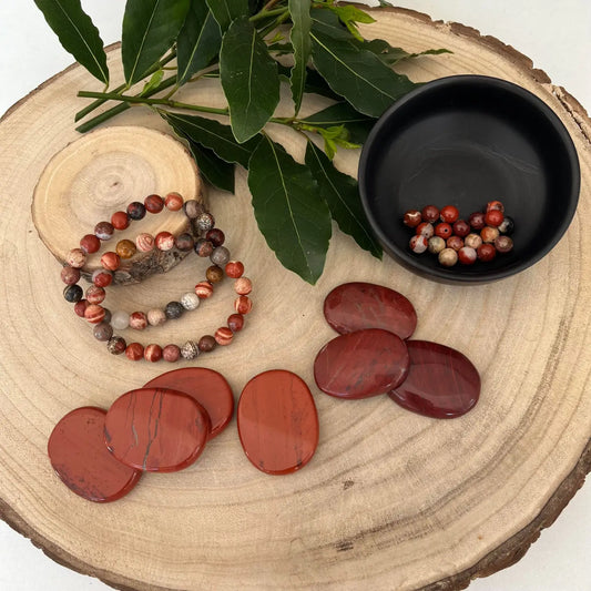 Exposition de jaspe rouge naturelle avec bracelets, pierres et accessoires en bois sur une table rustic.