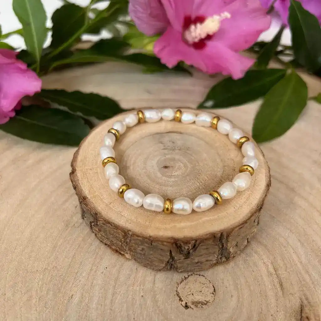Un bracelet avec des perles blanches irrégulières et de petites perles de couleur or.
