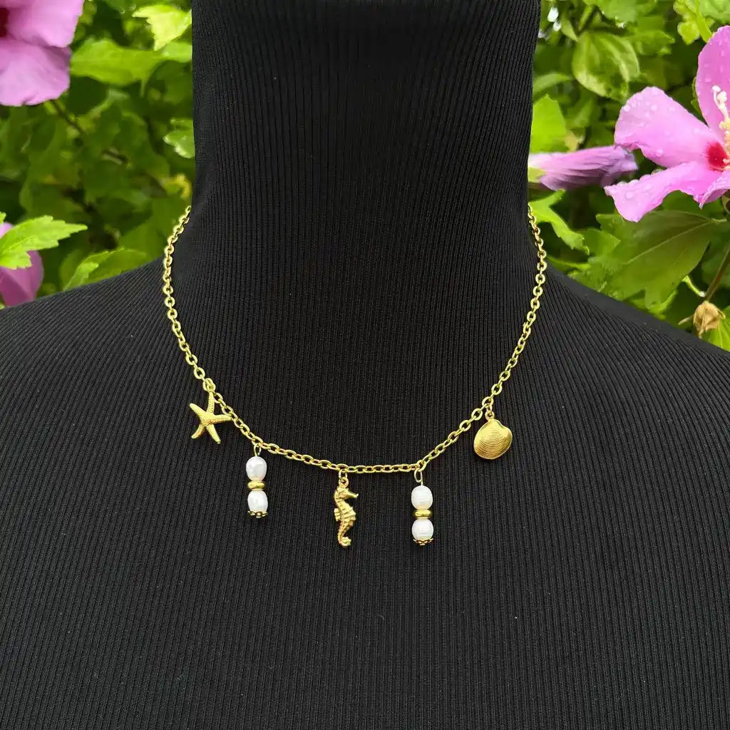 Un collier en or avec une étoile de mer, deux accents de perles, un hippocampe et un pendentif coquillage.