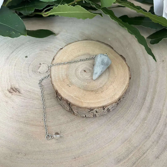 Pendule en Labradorite Aura de Roche pendentif conique en pierre posé sur tranche de bois avec chaîne argentée et feuillage