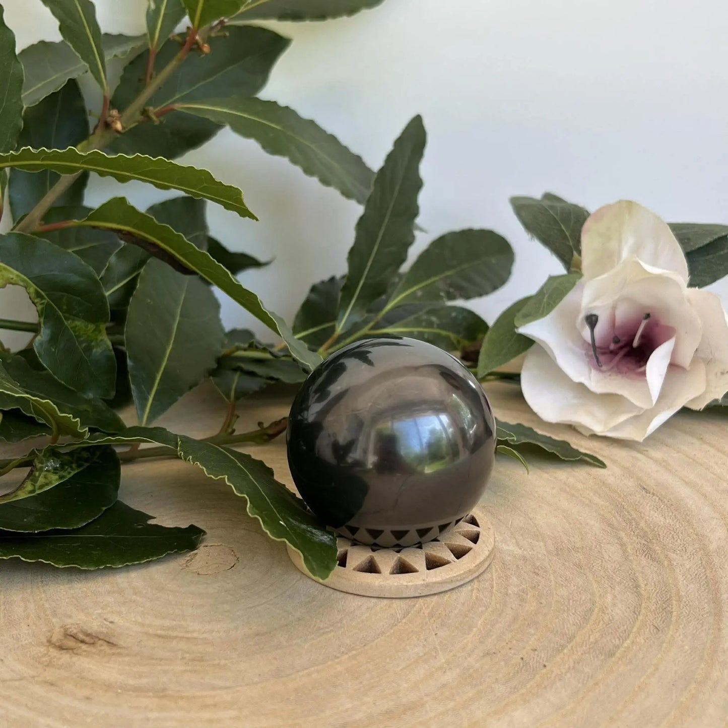 Sphère en shungite naturelle noire brillante posée sur un support en bois clair avec découpes triangulaires
