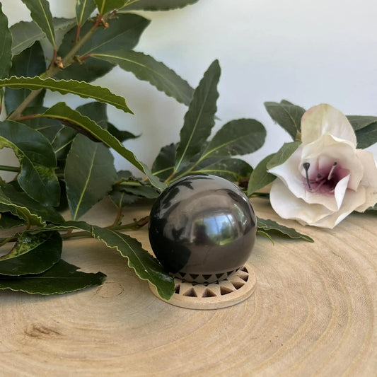 Sphère en shungite naturelle noire brillante posée sur un support en bois clair avec découpes triangulaires