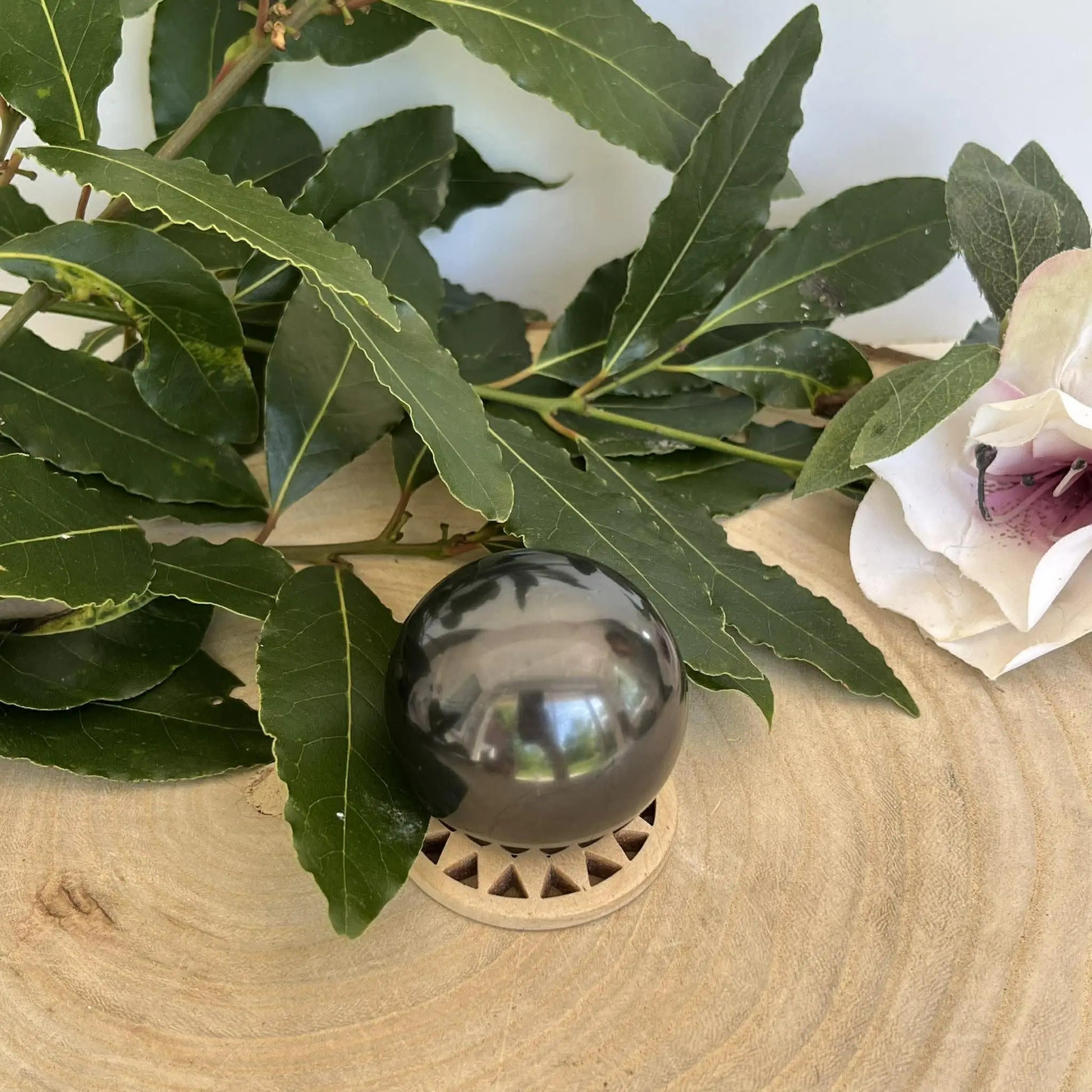 Sphère en shungite naturelle noire polie sur support en bois clair à découpes triangulaires pour protection et ancrage