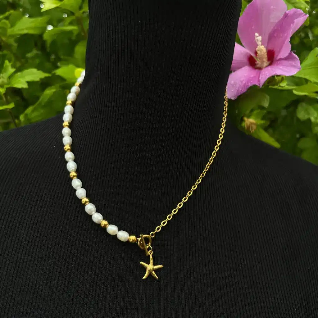 Un collier unique composé d'une moitié de perles blanches avec des accents dorés et l'autre moitié d'une chaîne en or simple, reliés par un pendentif étoile de mer en or.